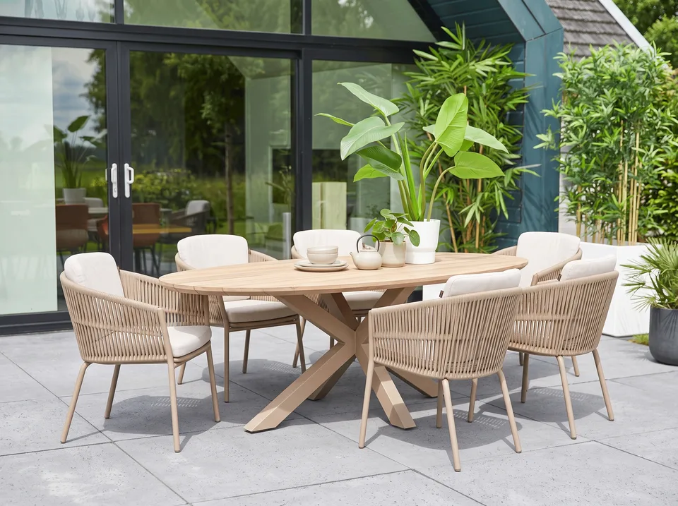 An oval teak garden table with chairs in front of a glass garden room